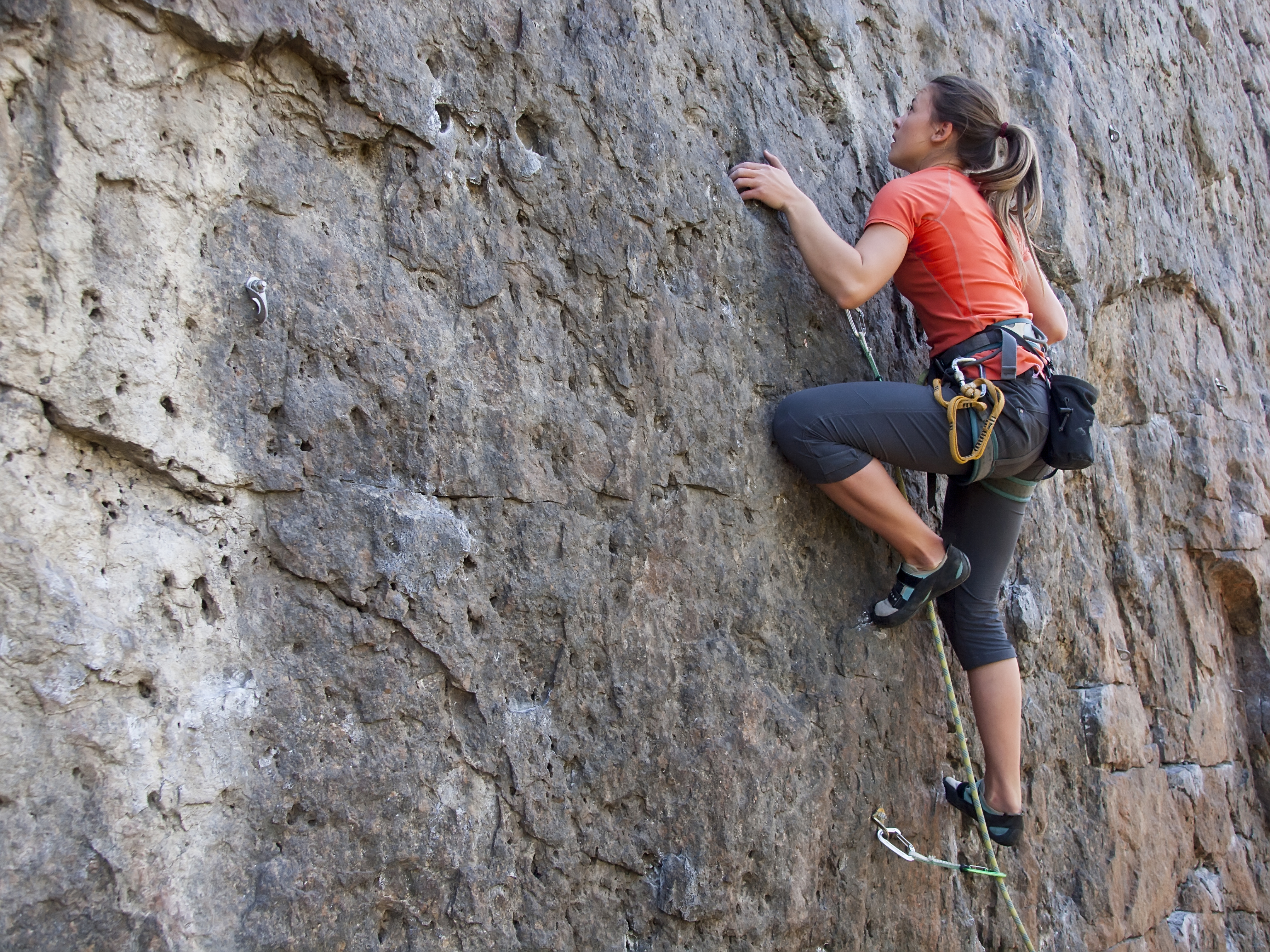 A young woman with a rope engaged in the sports of rock climbing on the rock.