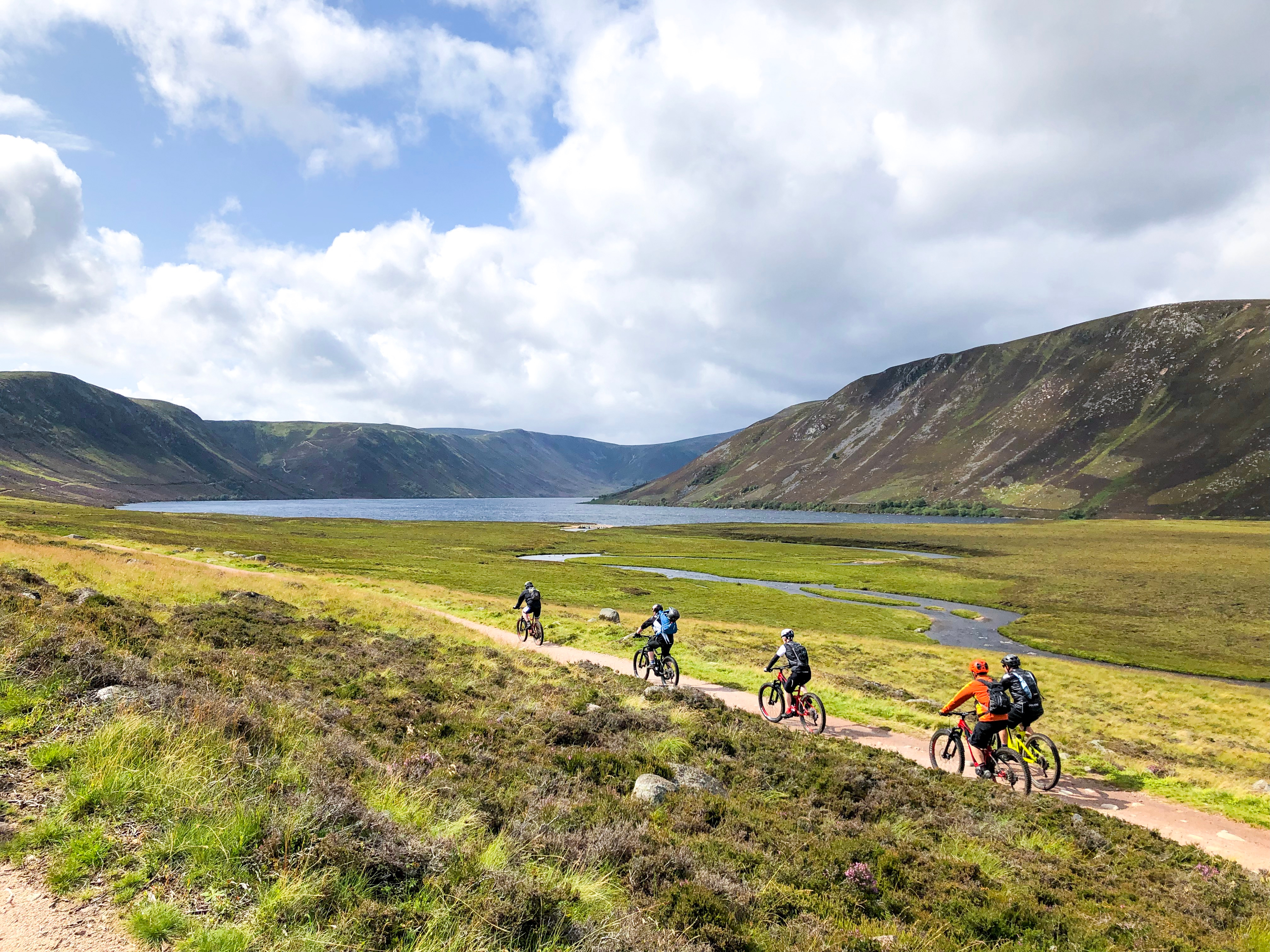 Group of people riding bicycles near a lake, lochnagar, during daytime, mountains appear in the background