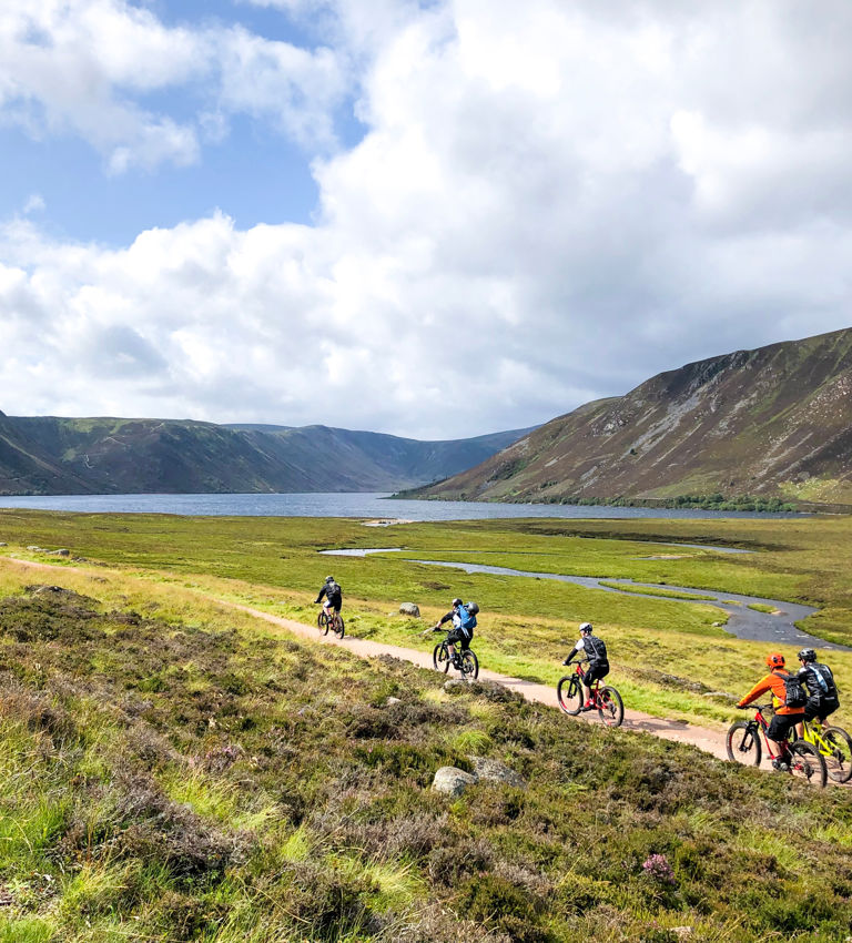 Group of people riding bicycles near a lake, lochnagar, during daytime, mountains appear in the background Group of people riding bicycles near a lake, lochnagar, during daytime, mountains appear in the background