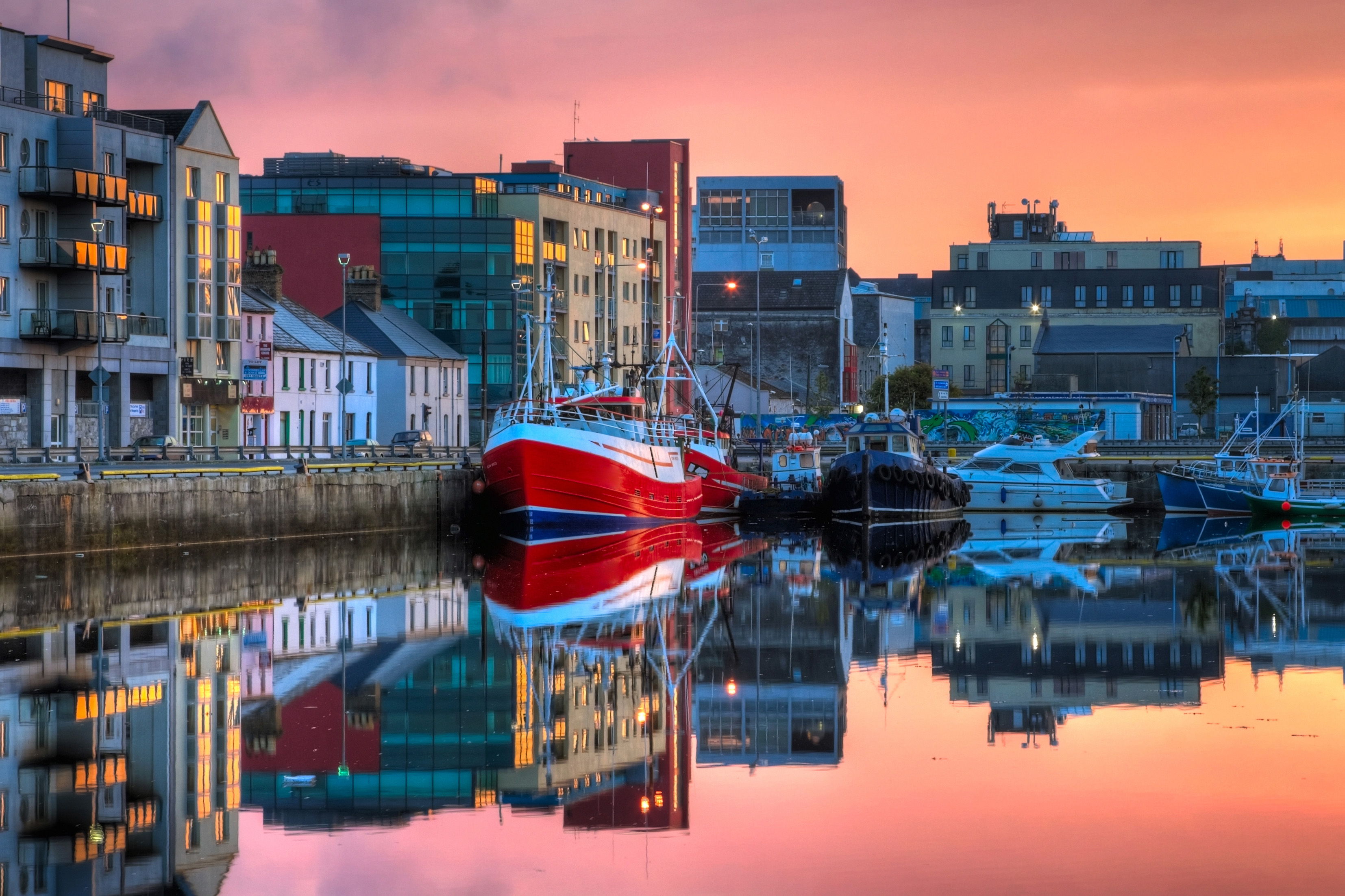 Morning view on row of buildings and fishing boats in Galway Dock with sky reflected in the water