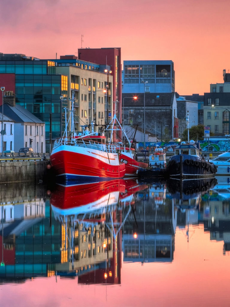 Morning view on row of buildings and fishing boats in Galway Dock with sky reflected in the water Morning view on row of buildings and fishing boats in Galway Dock with sky reflected in the water