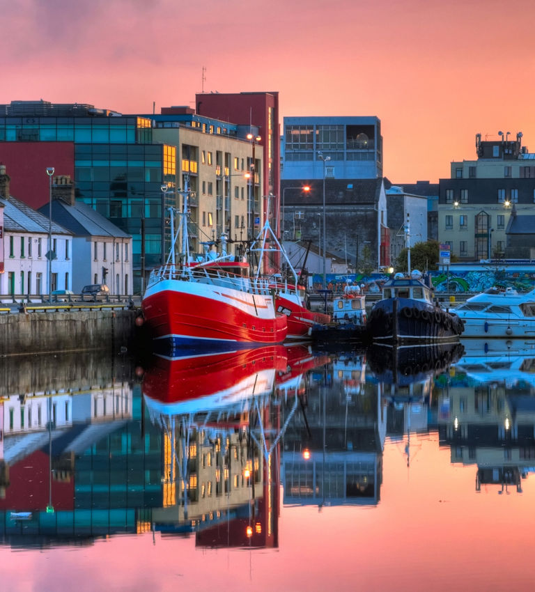 Morning view on row of buildings and fishing boats in Galway Dock with sky reflected in the water Morning view on row of buildings and fishing boats in Galway Dock with sky reflected in the water
