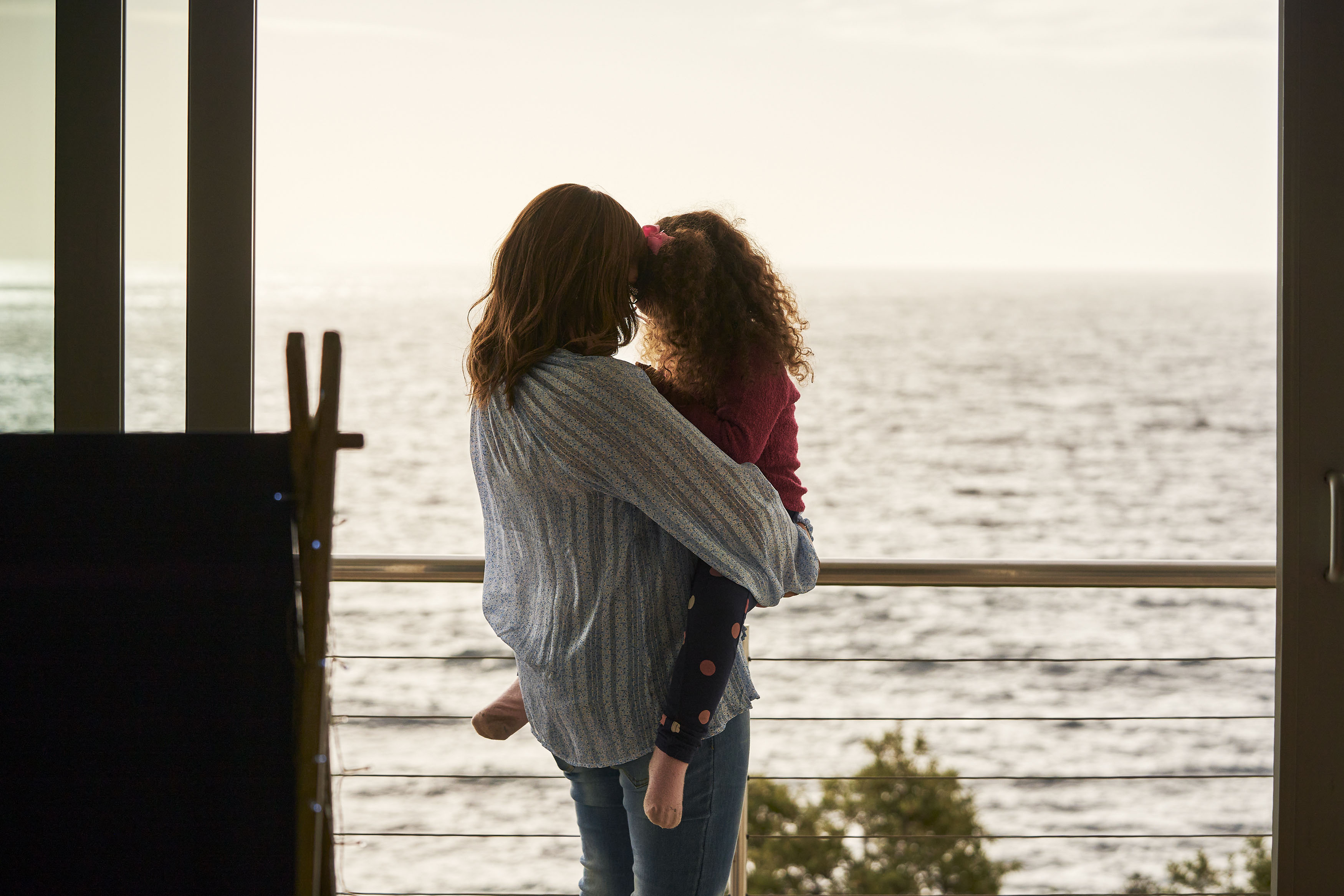 Mom holding daughter on balcony looking at the ocean