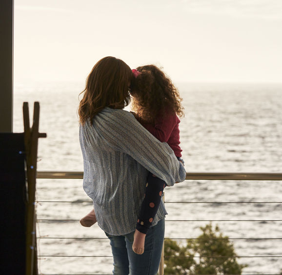 Mom holding daughter on balcony looking at the ocean Mom holding daughter on balcony looking at the ocean