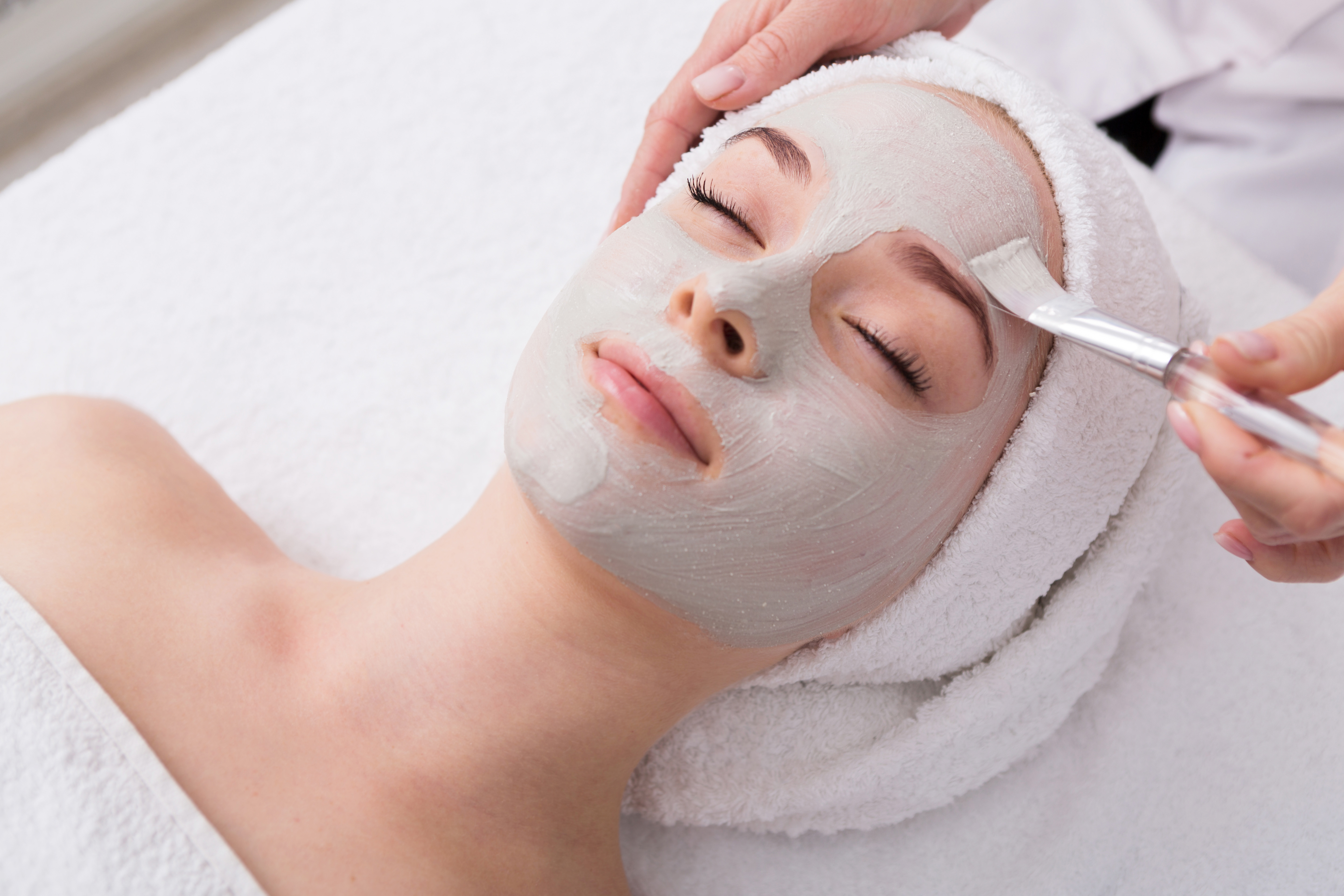 Face peeling mask, spa beauty treatment, skincare. Woman getting facial care by beautician at spa salon, side view, close-up