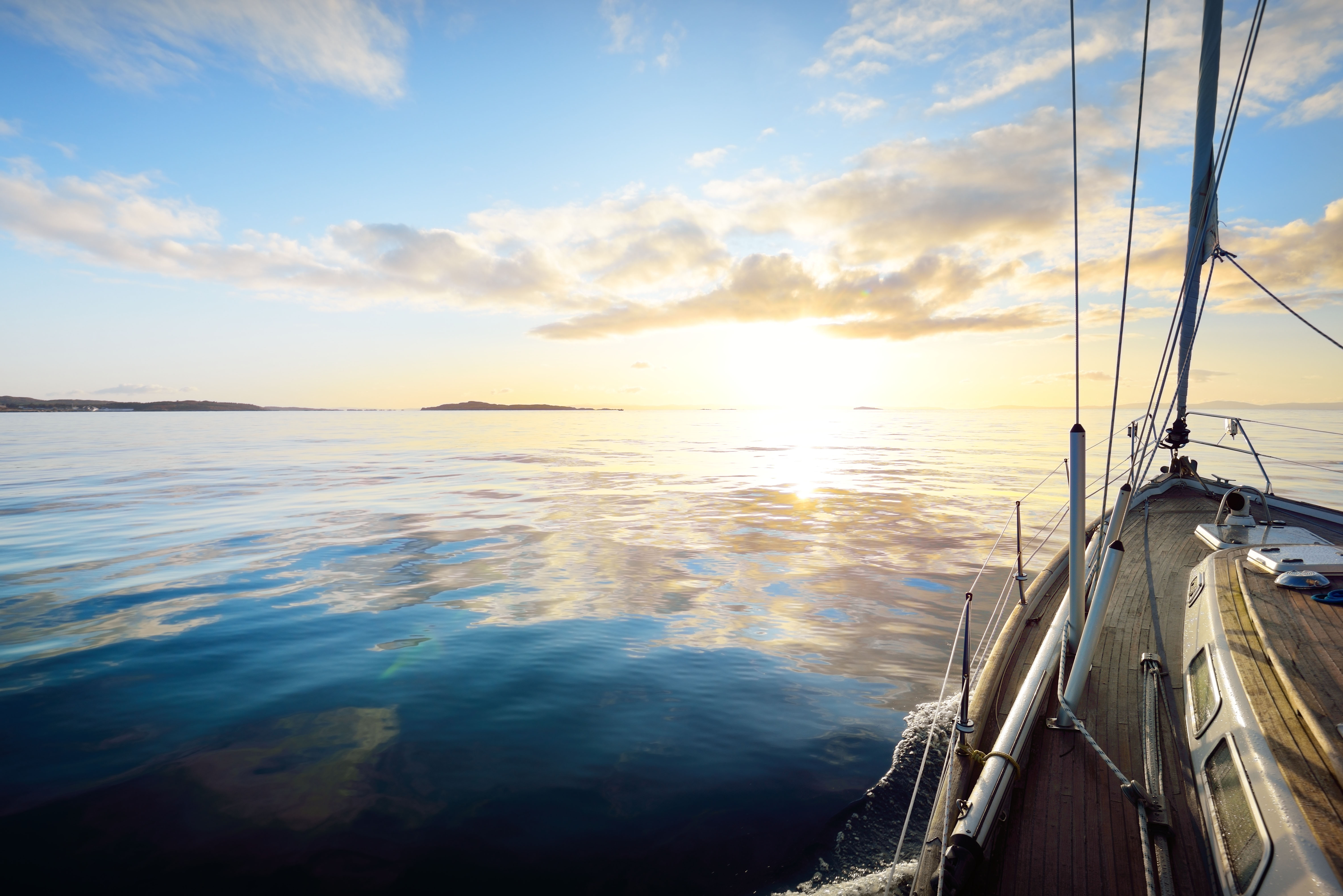 Sloop rigged modern yacht with wooden teak deck sailing at sunrise. A view from the deck to the bow. Colorful clouds. Port Ellen, Isle of Islay, Inner Hebrides, Scotland, UK Port Ellen, Isle of Islay, UK