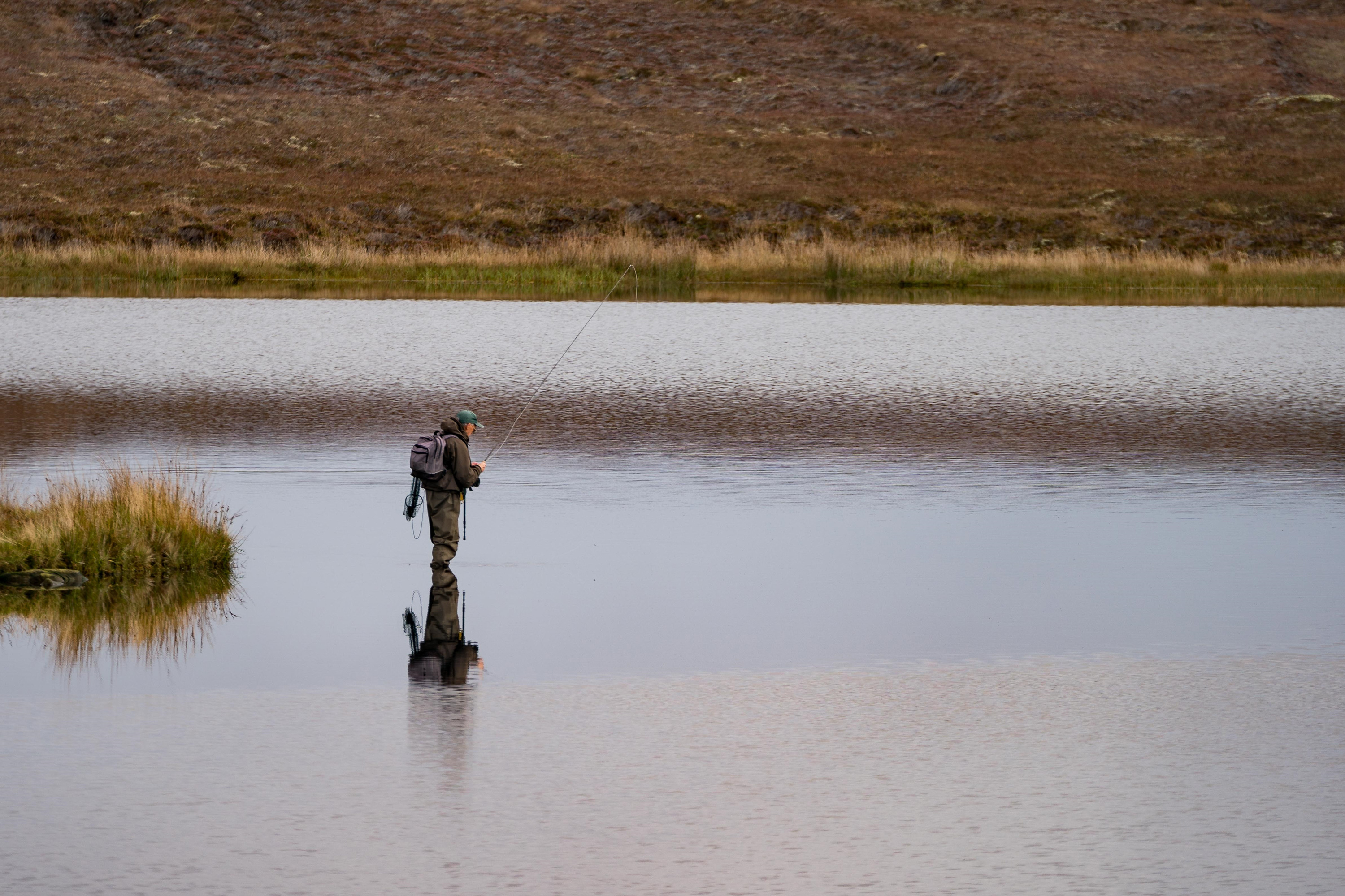 Fisherman alone stand in river water. Hobby sport activity. Fisherman fishing equipment. Reflection in Loch Long. Loch Long