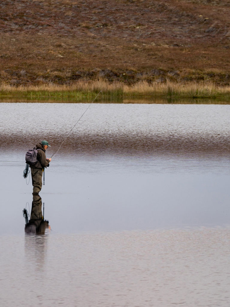 Fisherman alone stand in river water. Hobby sport activity. Fisherman fishing equipment. Reflection in Loch Long. Loch Long Fisherman alone stand in river water. Hobby sport activity. Fisherman fishing equipment. Reflection in Loch Long. Loch Long