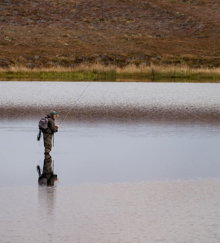 Fisherman alone stand in river water. Hobby sport activity. Fisherman fishing equipment. Reflection in Loch Long. Loch Long Fisherman alone stand in river water. Hobby sport activity. Fisherman fishing equipment. Reflection in Loch Long. Loch Long