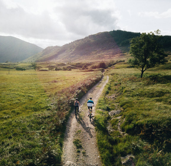 Couple cycling down a road in the Scottish Highlands Couple cycling down a road in the Scottish Highlands