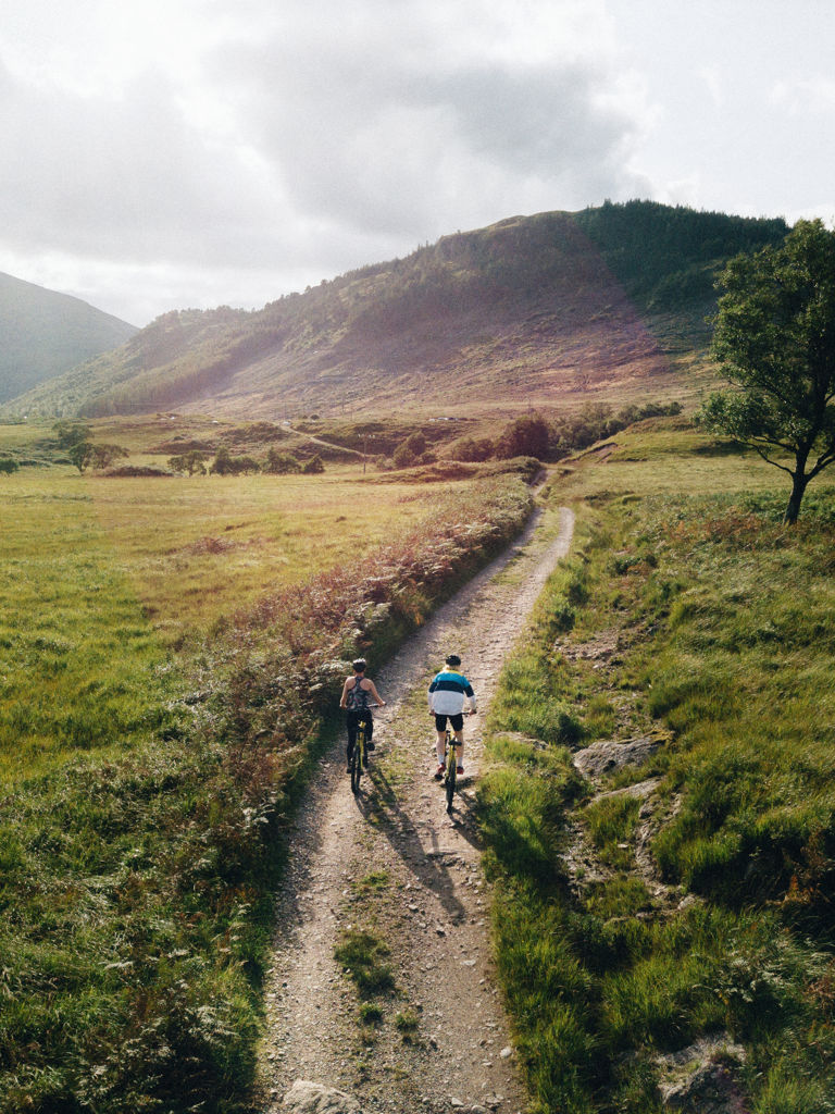 Couple cycling down a road in the Scottish Highlands Couple cycling down a road in the Scottish Highlands