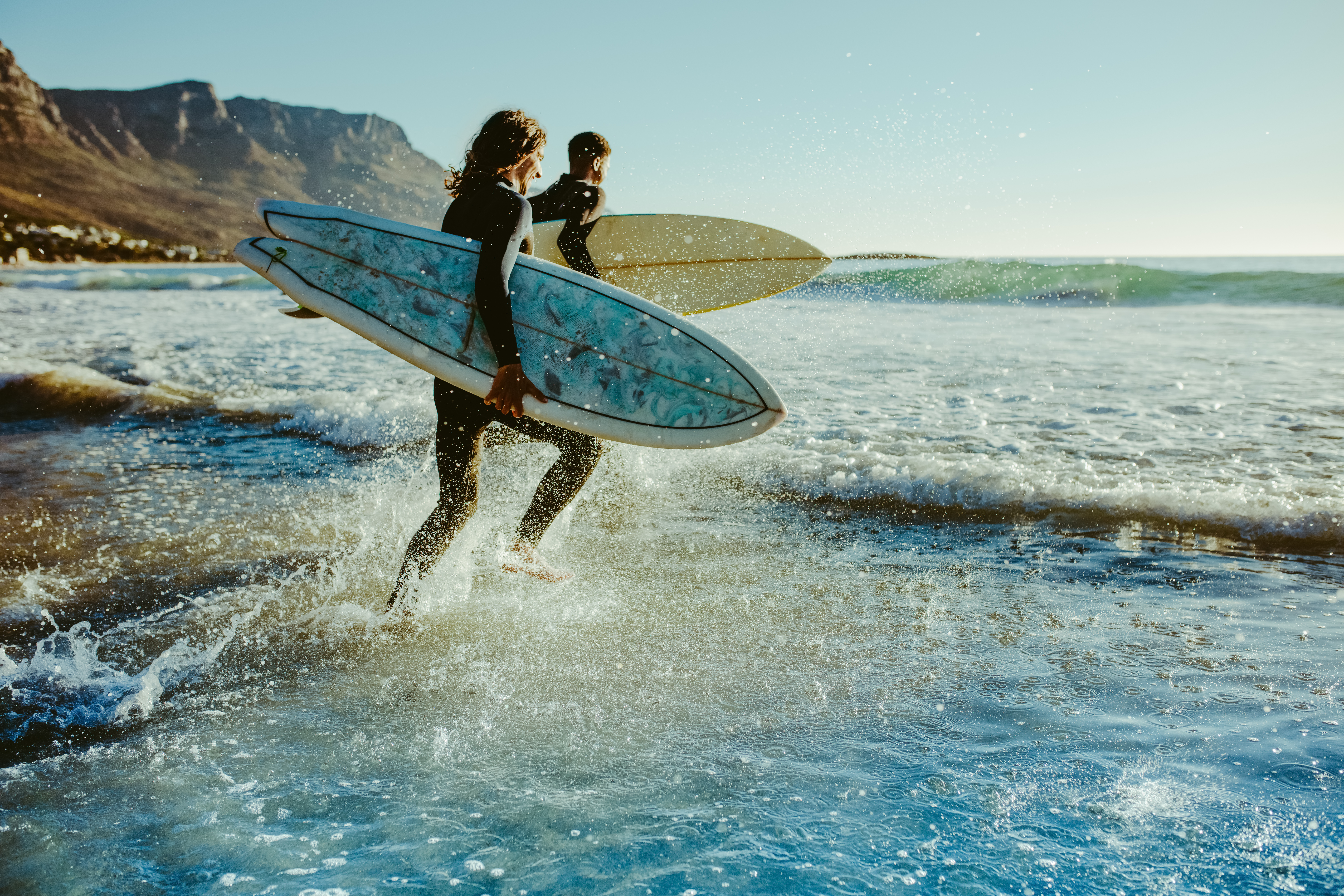 Two male surfers going for surfing in the sea. Two men carrying surfboards running in to the sea for surfing
