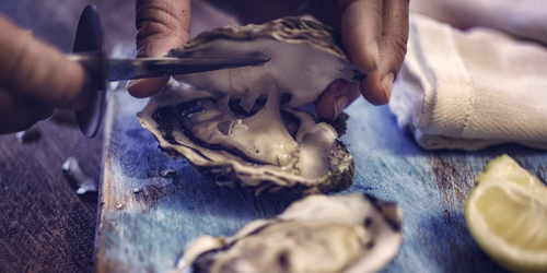 Man shucking oysters with a slice of cut lemon in the background