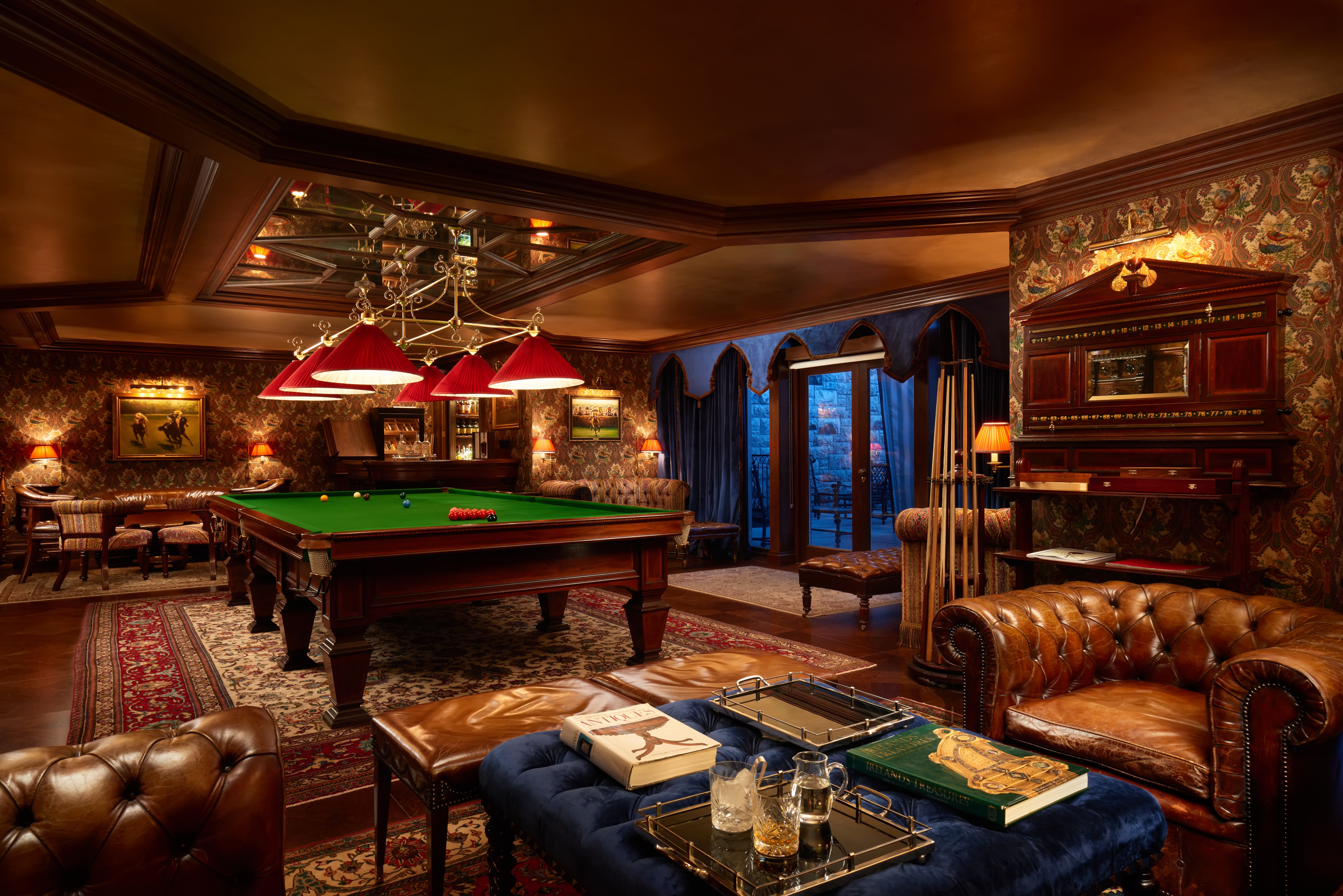 Billiards table with lounge area in the foreground with whiskey and books on a table
