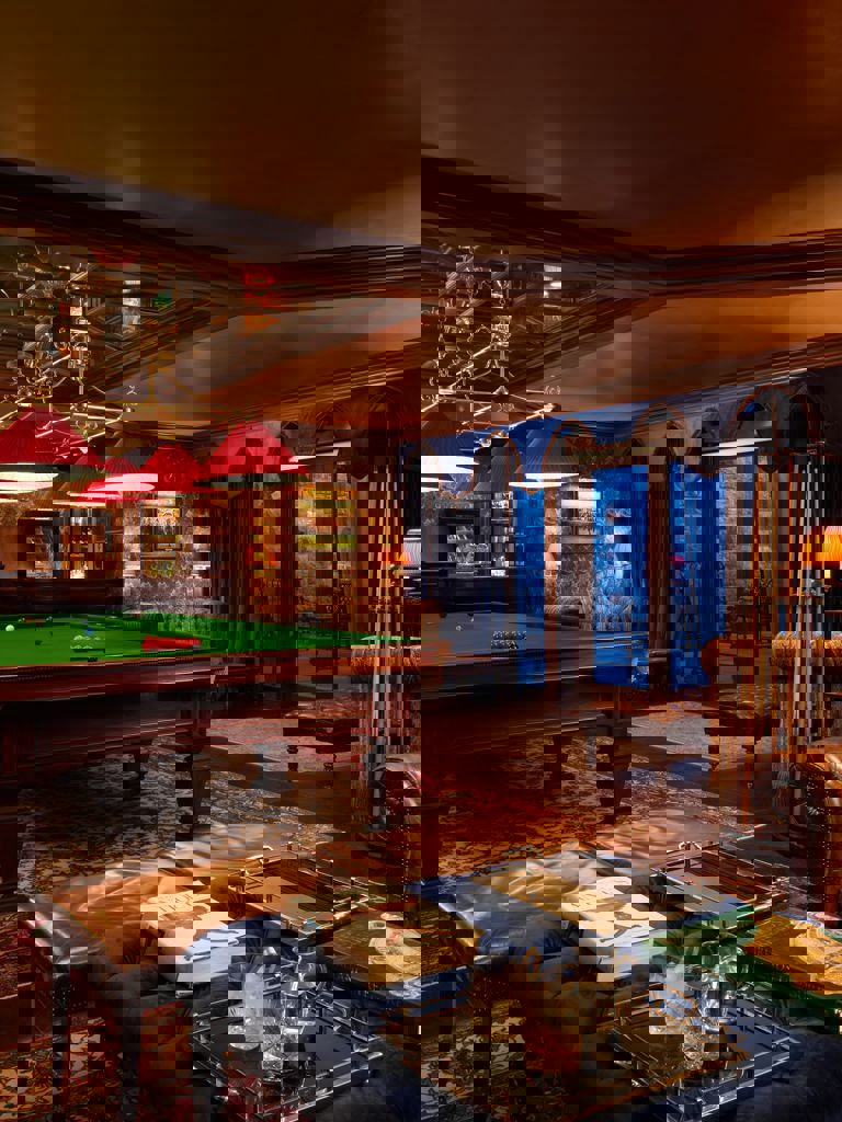 Billiards table with lounge area in the foreground with whiskey and books on a table Billiards table with lounge area in the foreground with whiskey and books on a table