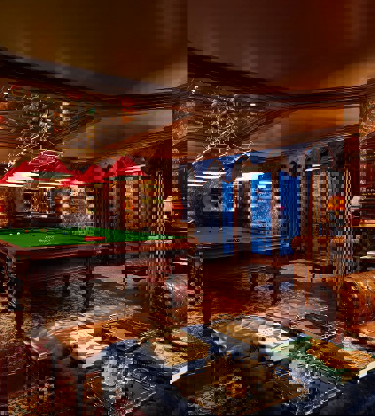 Billiards table with lounge area in the foreground with whiskey and books on a table Billiards table with lounge area in the foreground with whiskey and books on a table